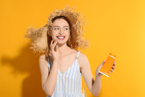 漂亮的年轻女子戴着草帽，拿着橙色背景的防晒霜图片下载