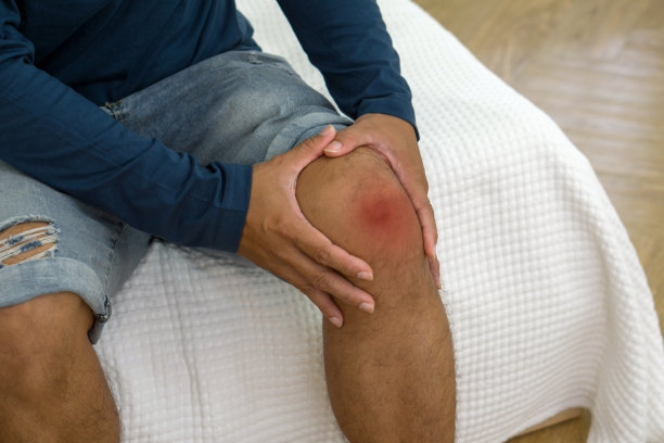 膝盖疼痛的受伤男子躺在室内的床上，表现出不适。近距离图片下载