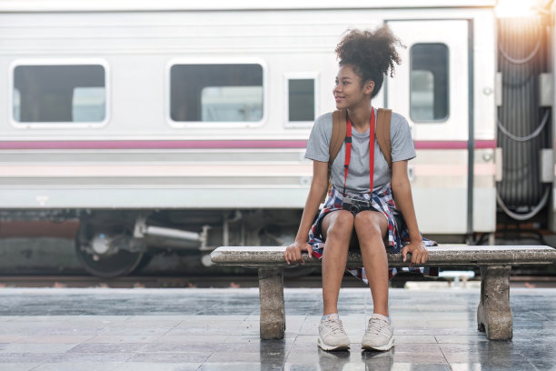 年轻的亚非女旅行者背着背包在火车站，旅行者女孩走着站着坐着等在火车站站台拍照。高质量照片图片下载