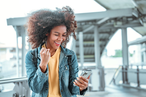 兴奋的年轻非裔美国女性在智能手机上阅读，为好消息感到高兴，女性在城市里为投资或银行应用程序欢呼时感觉像胜利者图片下载