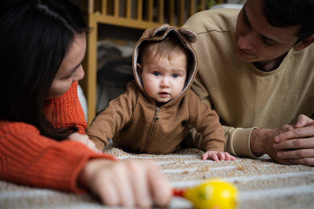 一男一女躺在地板上看着他们六个月大的女儿学着爬。儿童早期发展概念图片下载