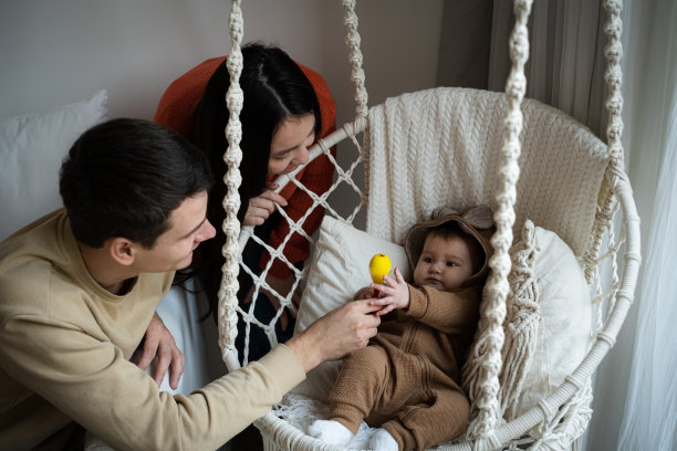 一个女人和一个男人在秋千上荡着他们五、六个月大的女婴。幸福家庭，为人父母，爱的观念图片下载