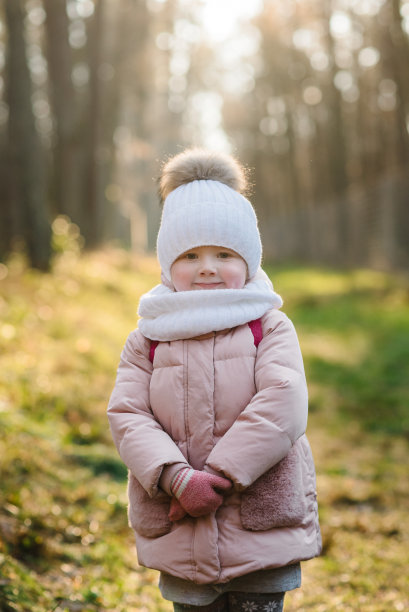 森林里，孩子站在金色散景阳光的背景下。快乐的女孩走在夕阳下的秋天公园。孩子们在树旁的街道上。秋天的照片，开始了冬天。孩子穿着暖和的衣服在户外散步。图片下载