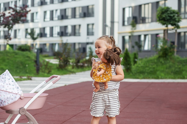 蹒跚学步的小女孩在玩玩具婴儿车和洋娃娃。两岁。发展的里程碑。图片下载