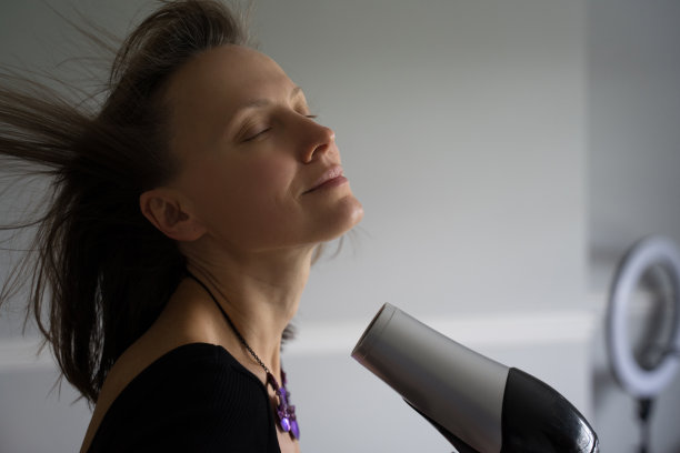 快乐微笑的女人在浴室里用吹风机图片下载