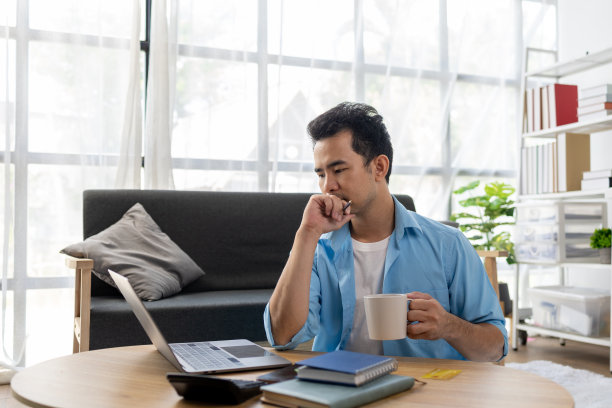 一名亚洲男子在家里的客厅里放松，他在周末放松，在空闲时间上网和浏览社交媒体。休息和周末的概念。图片下载