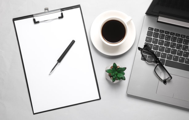 笔记本电脑，带有空白纸和咖啡杯的剪贴板，灰色背景的办公配件。平躺图片下载