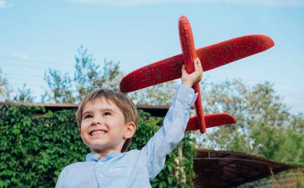 在绿色的花园里微笑的蹒跚学步的男孩。他在玩玩具飞机图片下载