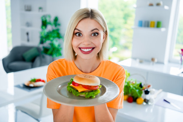 积极兴奋的女孩在家里餐厅做芝士汉堡的照片，为美食博客粉丝展示美味可口的小吃图片下载