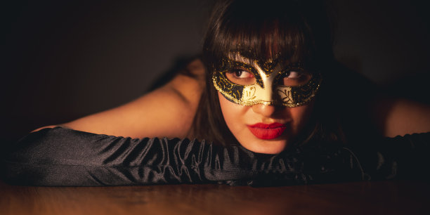 一个假面舞会的意大利女人坐在抛光的木地板上，戴着黑色手套，涂着红色唇膏。图片下载