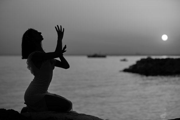 长发女士的剪影坐在岩石日落图片下载