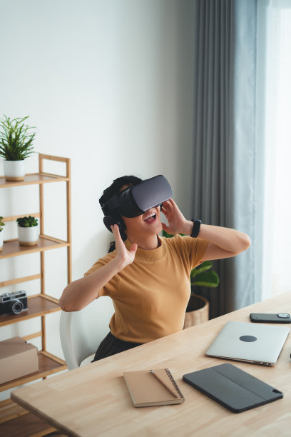 戴着VR耳机的亚洲女性在家办公室开心地微笑着。图片下载