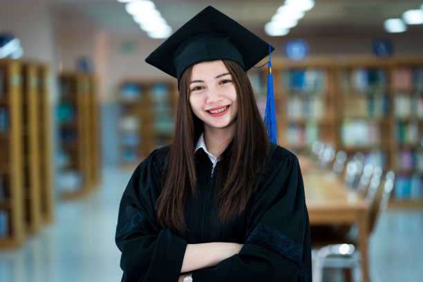 年轻快乐和兴奋的亚洲女大学毕业生穿着毕业礼服和毕业帽在图书馆。教育股票图片图片下载