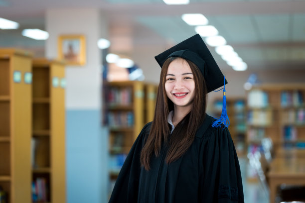 年轻快乐和兴奋的亚洲女大学毕业生穿着毕业礼服和毕业帽在图书馆。教育股票图片图片下载
