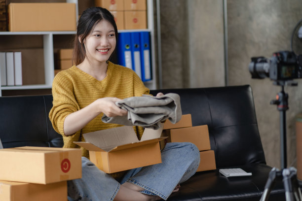 漂亮微笑的亚洲女人在家里用包裹箱网购，网上送货，小企业主。卖方正在准备寄给客户的包裹箱。网上销售或电子商务图片下载
