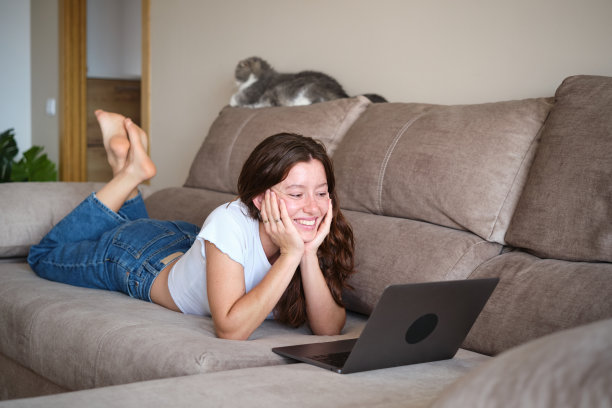 可爱的女人躺在家里的沙发上使用笔记本电脑图片下载