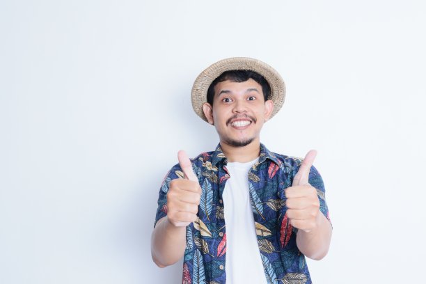 一个穿着沙滩装的年轻人的肖像，微笑着对着镜头竖起大拇指。度假旅游理念图片下载