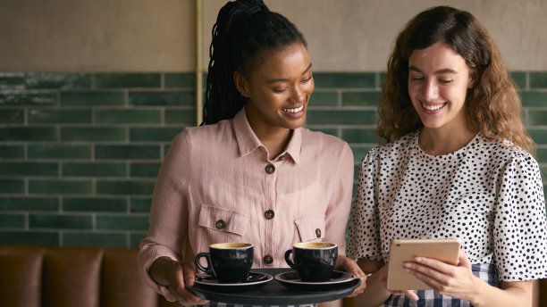 咖啡馆或咖啡店里两个微笑的女老板或员工拿着数码平板电脑和杯子图片下载