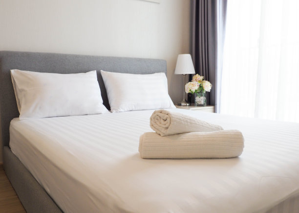 干净的白色床与白色枕头与模糊前景毛巾-家，舒适，旅游的概念图片下载