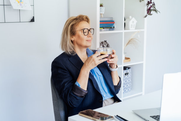 一位成功的、放松的、充满梦想的中年女商人正在她工作的地方休息，享受着咖啡休息时间。微笑自信的中年资深女性专业人士享受咖啡的味道。图片下载