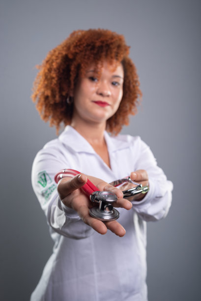 女兽医，漂亮的红头发，穿着白色制服对着镜头展示听诊器。图片下载