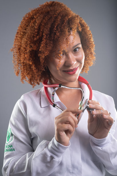 一个红头发的女兽医的画像，穿着白色的制服，把听诊器靠近她的脸。动物保健。图片下载