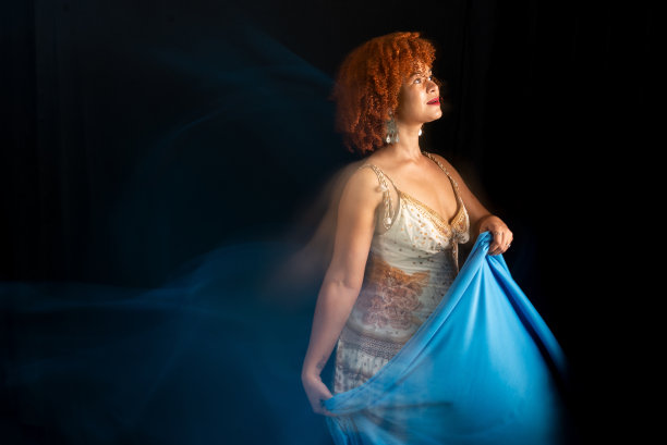 这张照片是以低速拍摄的，一个美丽的女人，她有着卷曲的红头发，正在用一块蓝色的布做动作图片下载