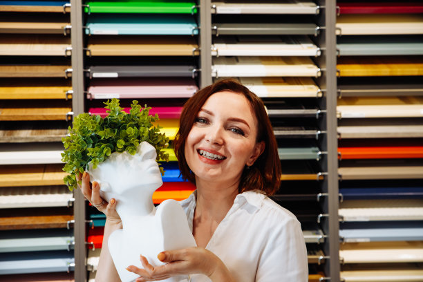 年轻的微笑着的女性，拿着白色的花瓶头，手里拿着树叶，站在五颜六色的样品墙上。36岁白人女性肖像。室内设计师、建筑师、女商人图片下载