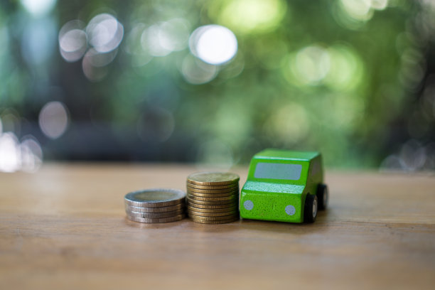 绿色玩具车和堆钱堆硬币增长。交通保险汽车护理行业概念。图片下载
