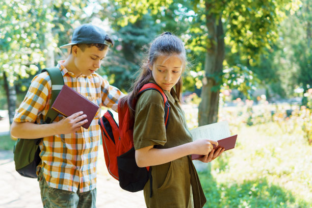 学校的学生，一个十几岁的男孩和一个女孩走在街上，玩得很开心，聊天，看书，一个明媚的夏日在城市公园，一条小路和树叶图片下载