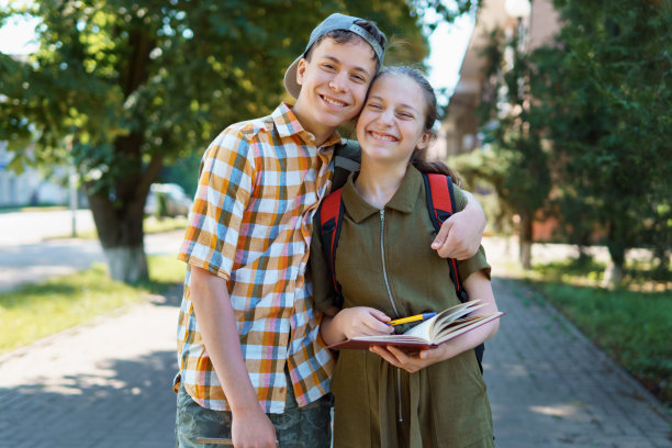 学生，一个十几岁的男孩和一个女孩走在街上，玩得开心，聊天，看书，一个明媚的夏日在城市公园图片下载