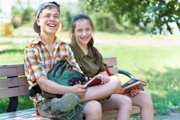 小学生，一个十几岁的男孩和一个女孩坐在城市公园的长凳上，聊天，看书，做作业，这是一个明媚的夏日图片下载