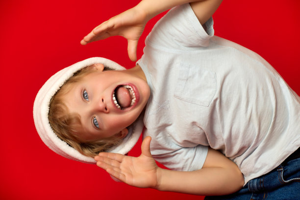 一个戴着圣诞帽的有趣的孩子在红色背景的镜头前扭动图片下载
