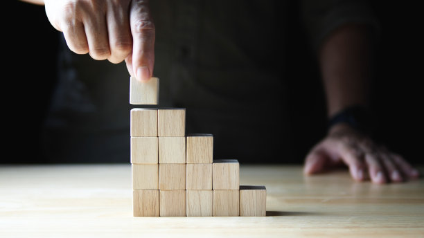 企业发展走向成功。商人手堆木块做台阶，生意成长成功在黑暗的背景下。业务增长的概念，财务规划，投资，战略图片下载