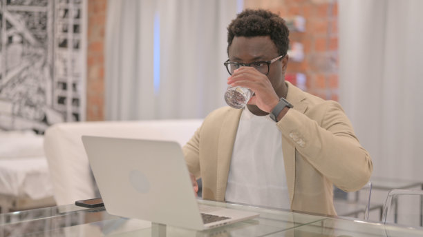 非裔美国人一边用笔记本电脑工作一边喝水图片下载