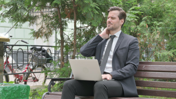 颈部疼痛的中年商人在户外用笔记本电脑工作图片下载