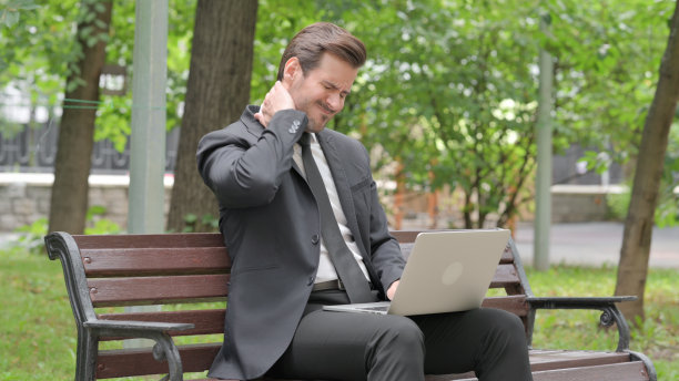 颈部疼痛的年轻商人在户外用笔记本电脑工作图片下载