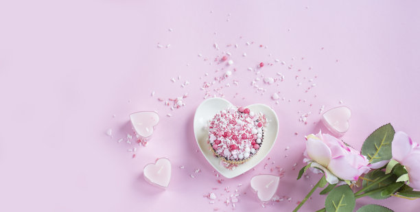 纸杯蛋糕放在盘子里，粉红色的背景上有一颗心。粉红色的玫瑰。横幅图片下载