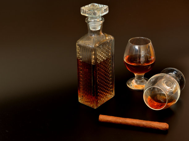 两杯干邑，一杯水晶酒瓶和一支黑色背景的古巴雪茄。图片下载