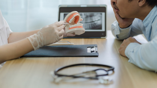 戴橡胶手套的女牙医在诊所为牙痛的男病人进行牙齿健康检查，以牙科模型为指导，以x光片成像，口腔保健概念图片下载