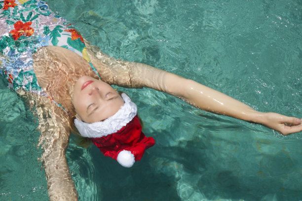 戴着圣诞帽的年轻女子在游泳池里放松。圣诞热带度假概念。图片下载