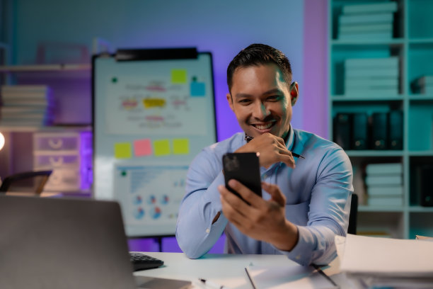 一位坚定的亚洲商人正在使用智能手机，在办公室加班到深夜。图片下载