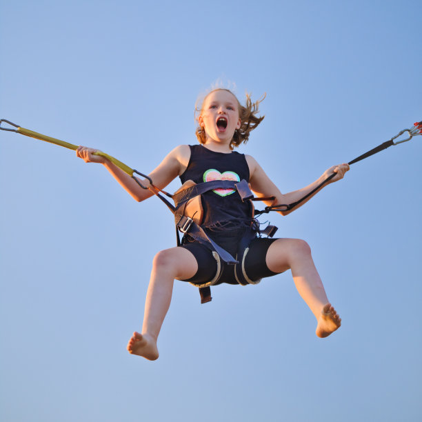 在游乐园和旋转木马上，小女孩用保险橡皮筋在蹦床上蹦蹦跳跳。图片下载