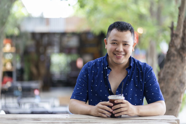 一名亚洲男子悠闲地坐着，用塑料杯喝着冰咖啡。图片下载