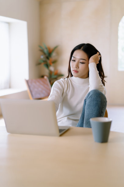 心烦意乱的美丽亚洲女性自由职业者坐在家里的办公桌上使用笔记本电脑，感到疲倦，担心新项目的问题，感到沮丧，在家里办公室办公桌在寒假期间懒惰。图片下载