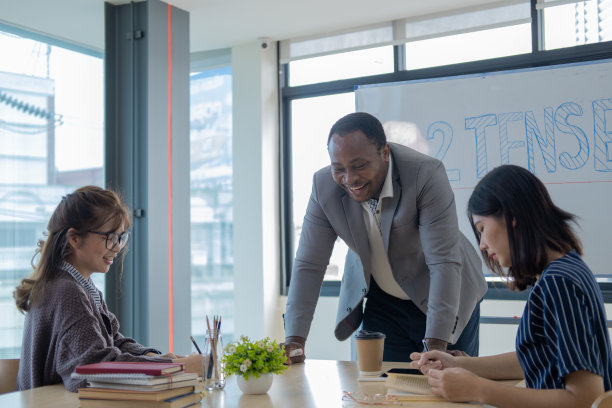 男老师带着两个十几岁的学生坐在大学的课桌前学习，两个女生坐在教室旁边，一个男老师拿着白板教学图片下载