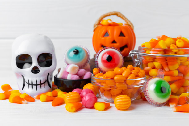 万圣节糖果玉米，果冻眼，南瓜糖，糖头骨在不同的碗背景。万圣节的经典糖果。万圣节的概念是玉米糖和南瓜灯。图片下载