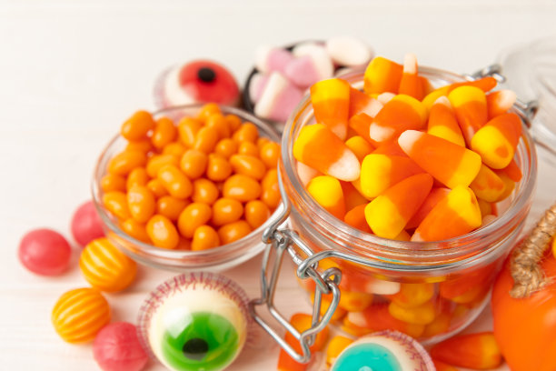 万圣节糖果玉米，果冻眼，南瓜糖，糖头骨在不同的碗背景。万圣节的经典糖果。万圣节的概念是玉米糖和南瓜灯。图片下载
