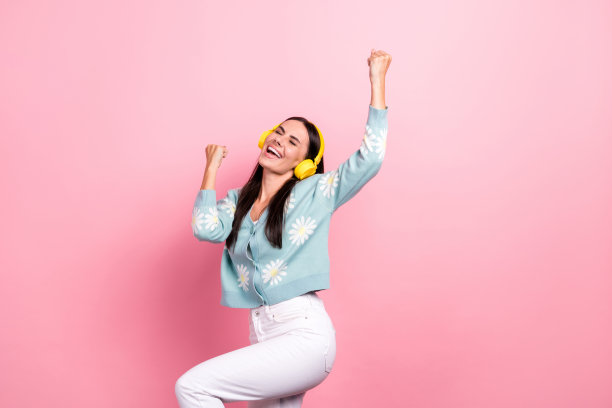 照片中时髦的幸运女子穿着蓝色开衫跳舞唱歌，举起拳头孤立的粉红色背景图片下载