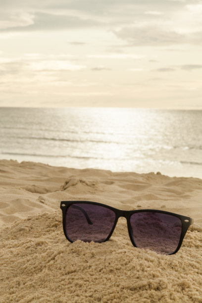 太阳眼镜放在沙滩上，背景是海的地平线，阳光反射在海浪上。图片下载